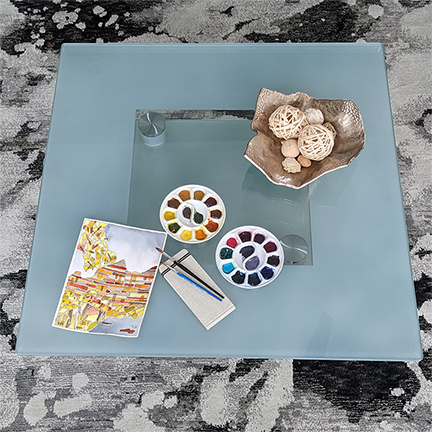 table with water color painting, sketchbook, brushes, and paint pallets